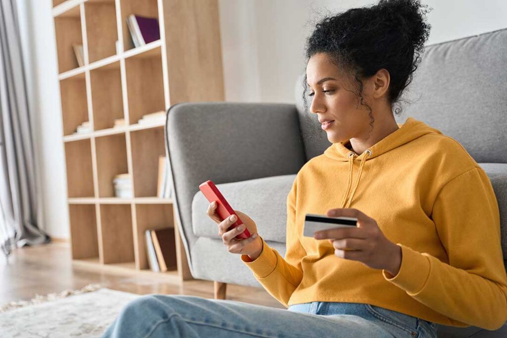 A person reviews a secure banking app on a smartphone beside a laptop and household bills.